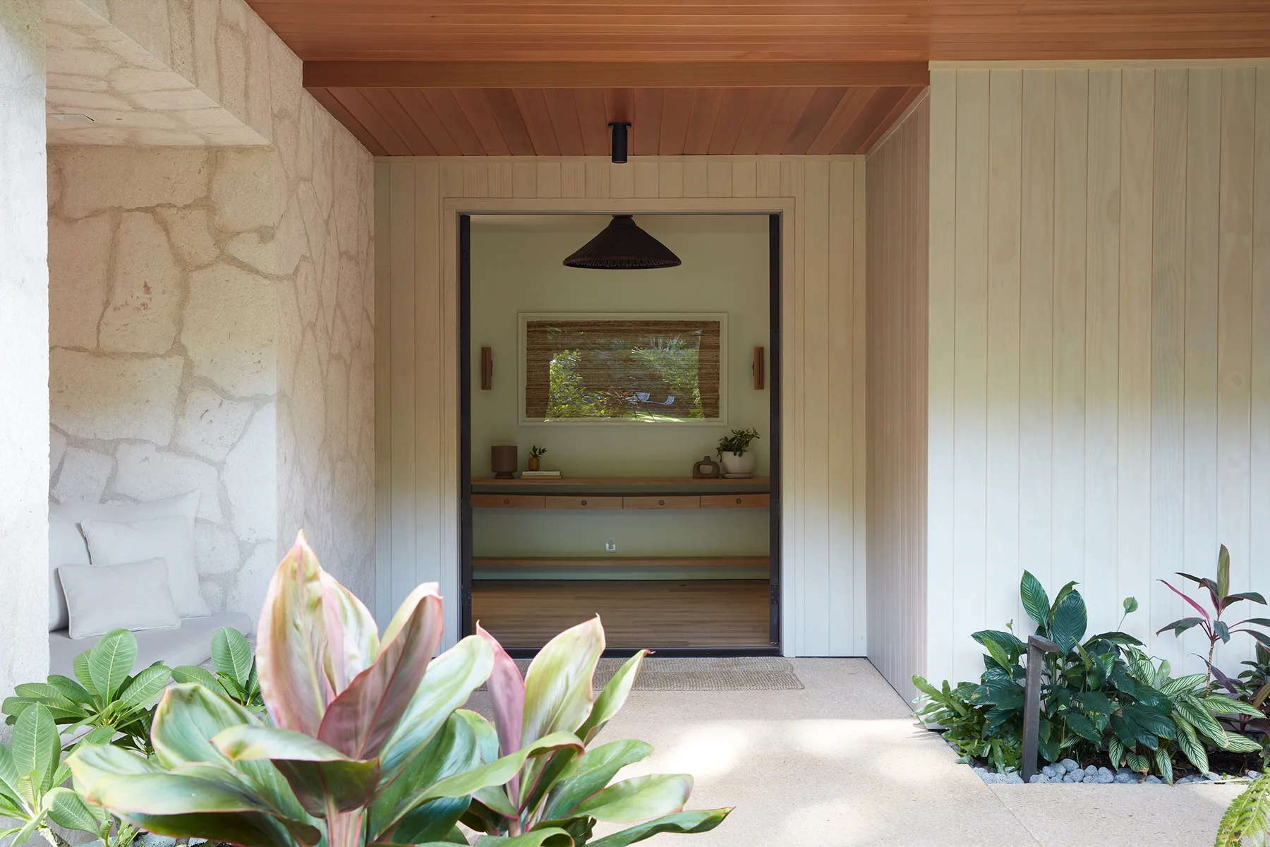 A garden-facing entrance opens onto a wood-paneled interior with plants along the path.