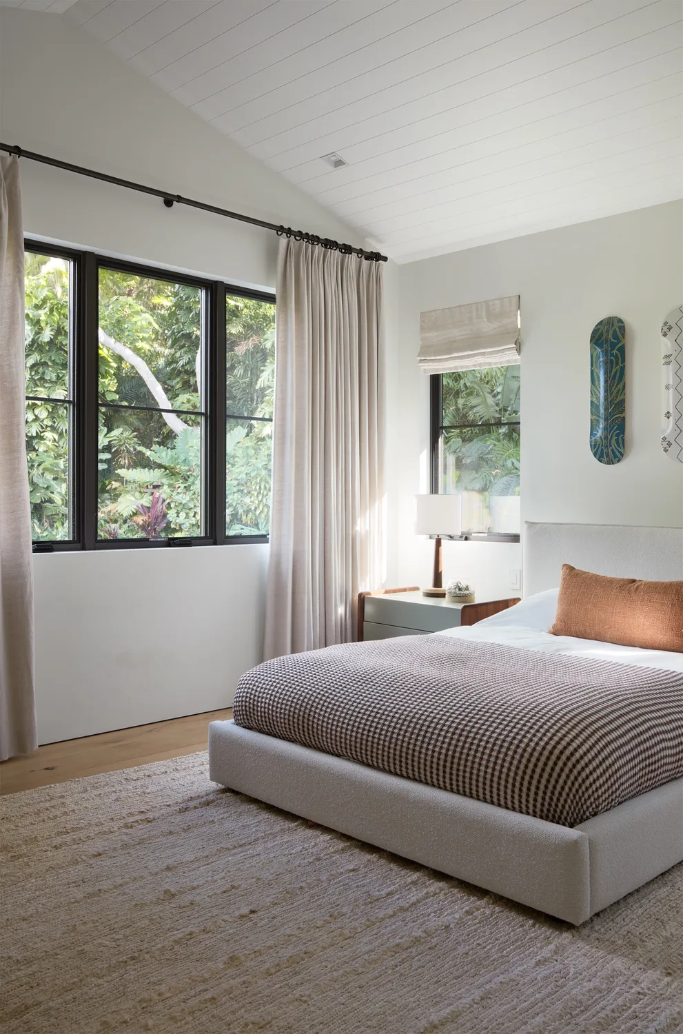 A bright bedroom with a bed beside large windows overlooking greenery.