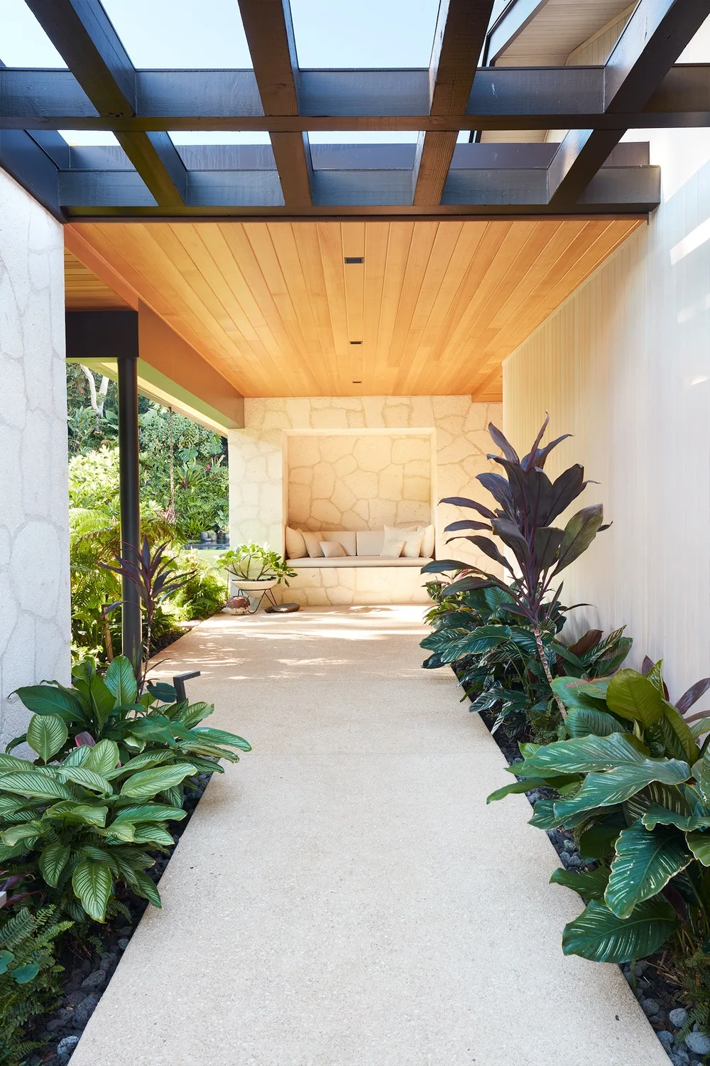 A covered outdoor walkway with a built-in bench and leafy plants.