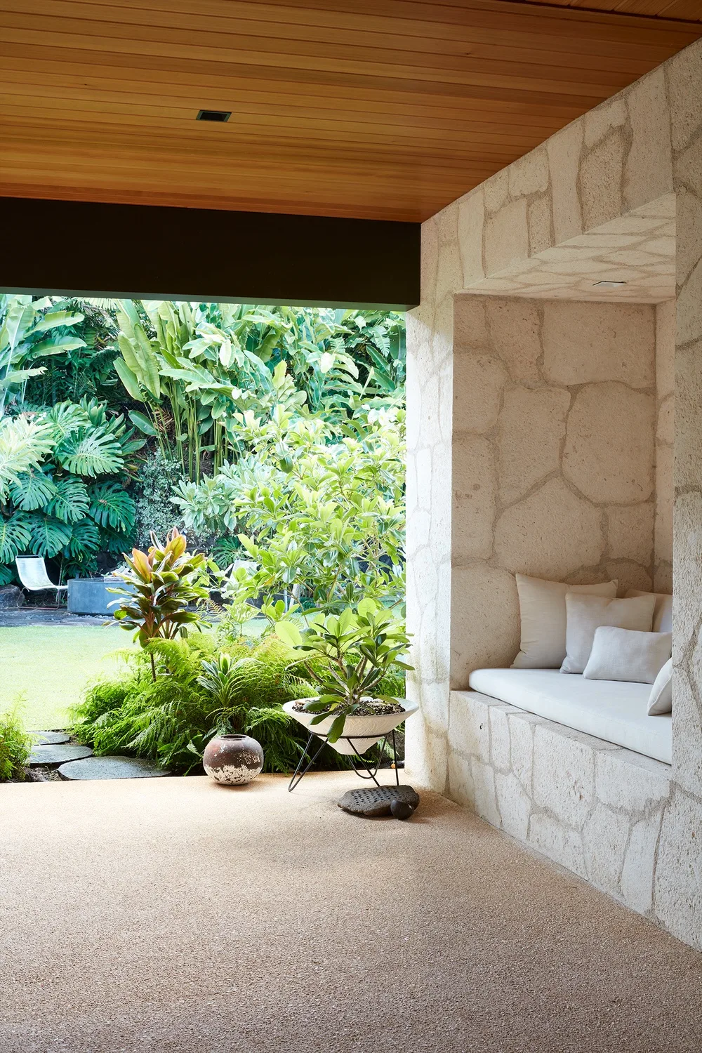 A covered patio opens onto a lush garden, with built-in seating along the stone wall.
