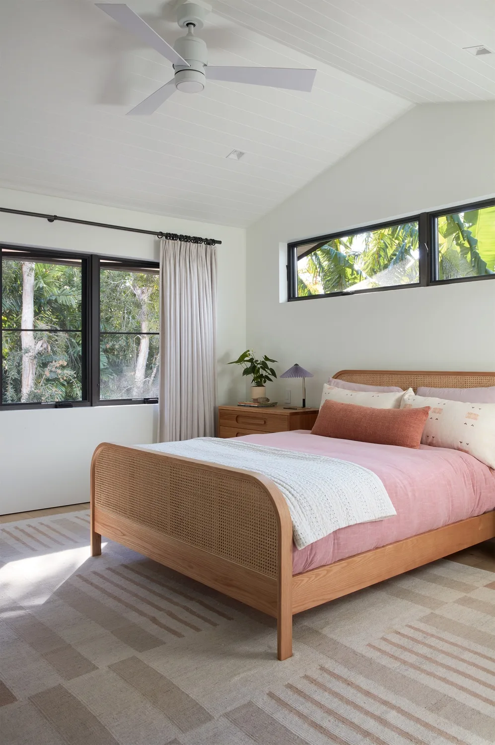 A bright bedroom with a wooden bed dressed in pink and white bedding.