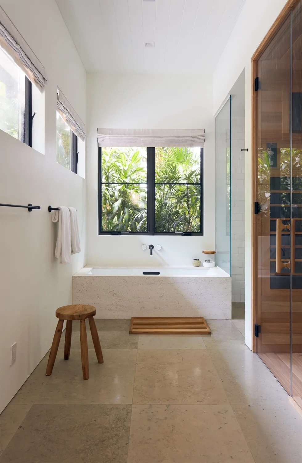 A bright bathroom with a bathtub beneath a large window overlooking greenery.