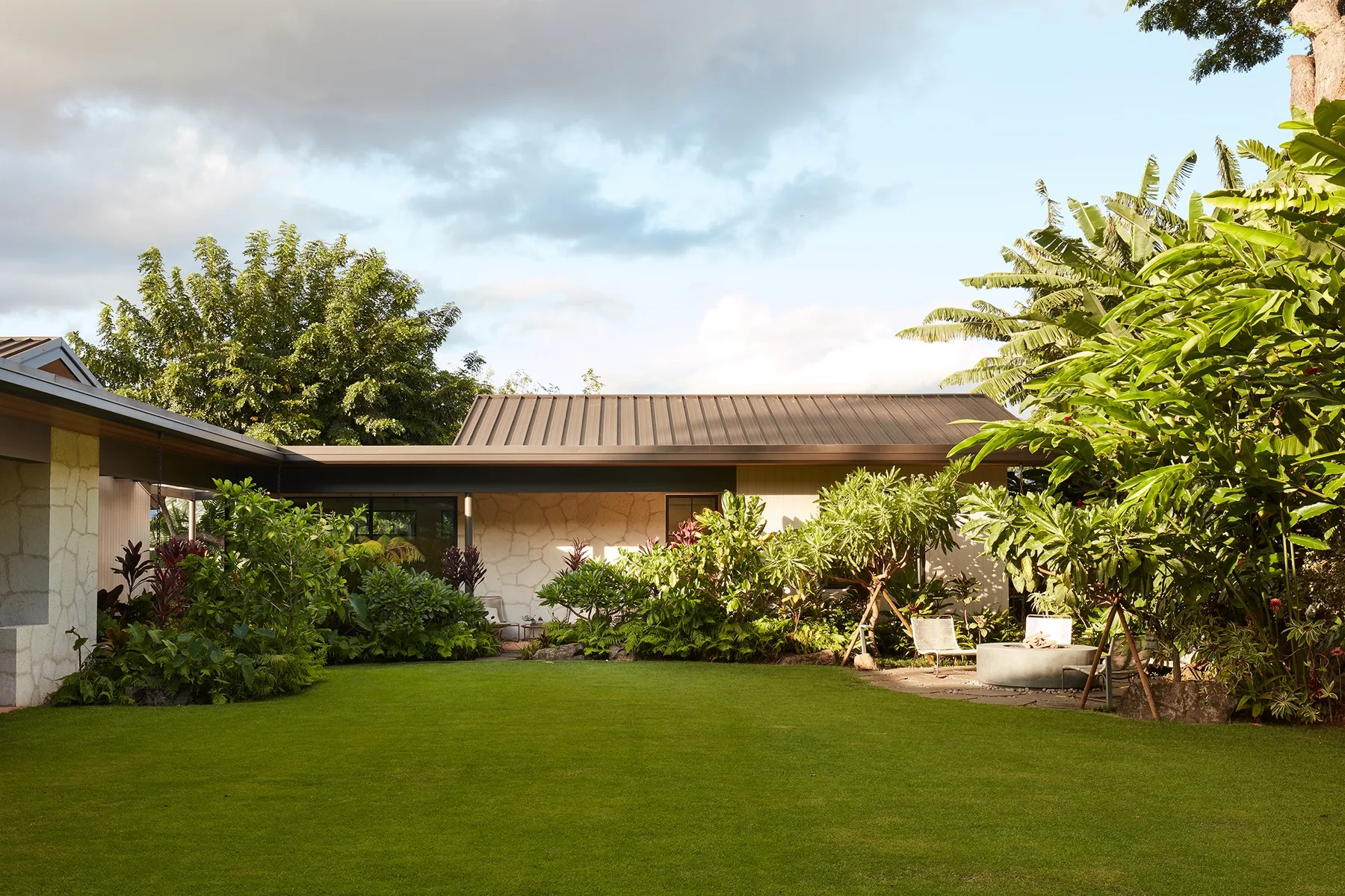 A landscaped garden lawn bordered by a low building and tropical plants.