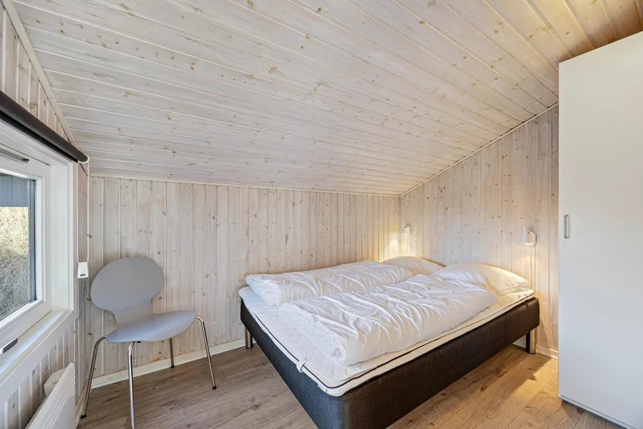 Un dormitorio con una cama, una silla y una ventana bajo un techo de madera inclinado.