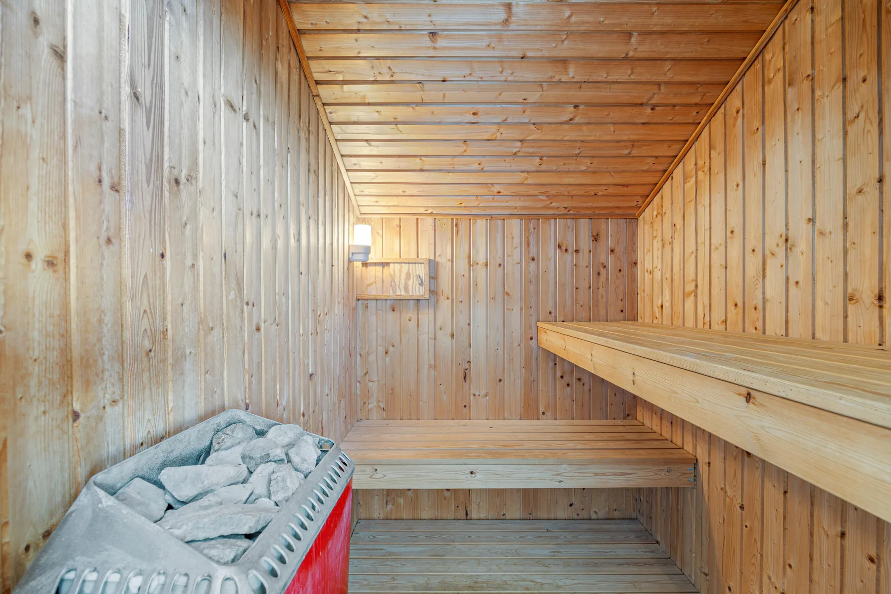 Una sauna revestida de madera con asientos escalonados y un calentador de piedras.