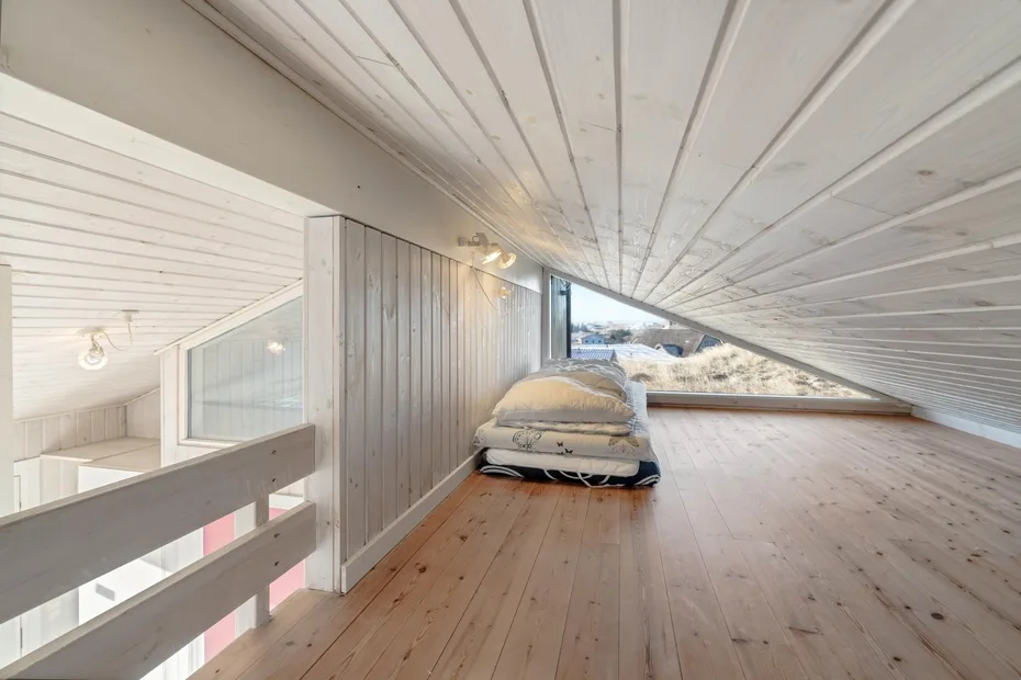 Un dormitorio tipo loft luminoso con una cama bajo un techo blanco inclinado.