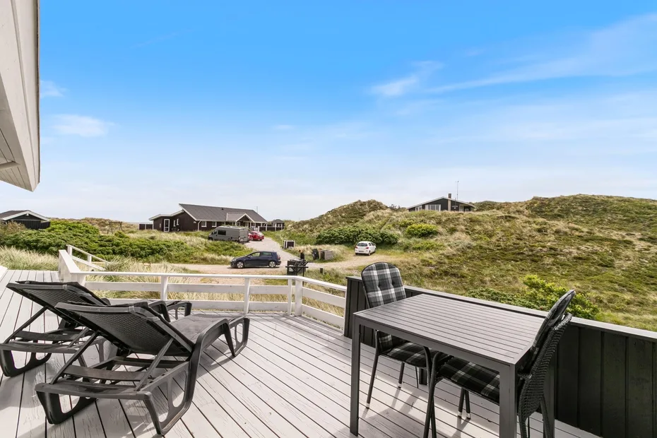 Una terraza exterior con muebles de comedor da a dunas cubiertas de hierba y casas cercanas.