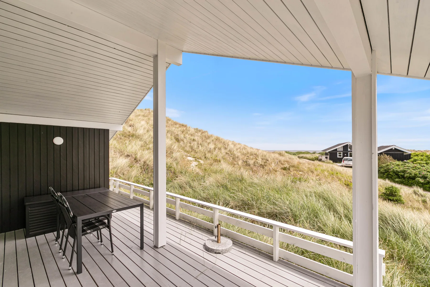 Un patio cubierto con asientos al aire libre da a dunas cubiertas de hierba y casas cercanas.