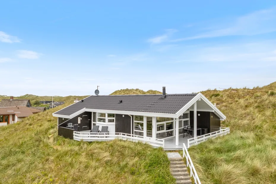 Una casa moderna está entre dunas cubiertas de hierba bajo un cielo azul despejado.
