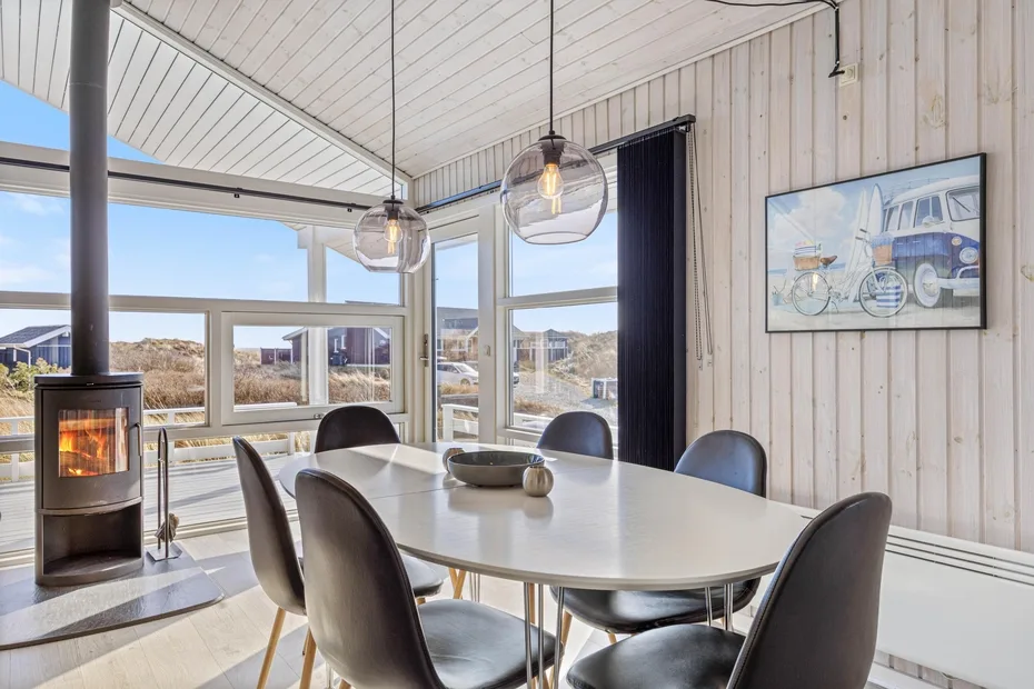 Un comedor luminoso con una mesa larga, asientos y grandes ventanas con vistas al paisaje.