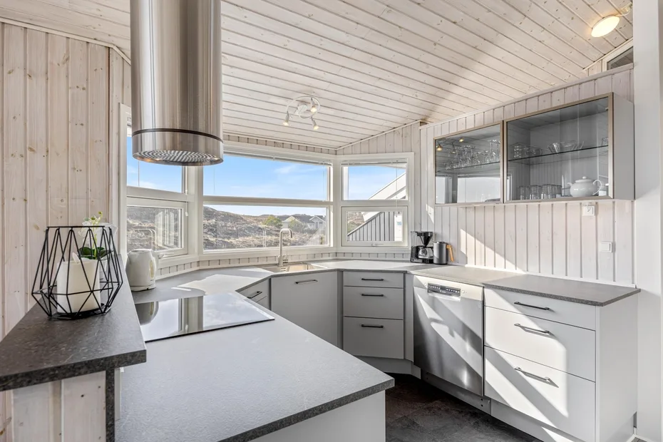 Una cocina luminosa con gabinetes blancos, encimeras oscuras y ventanas amplias.