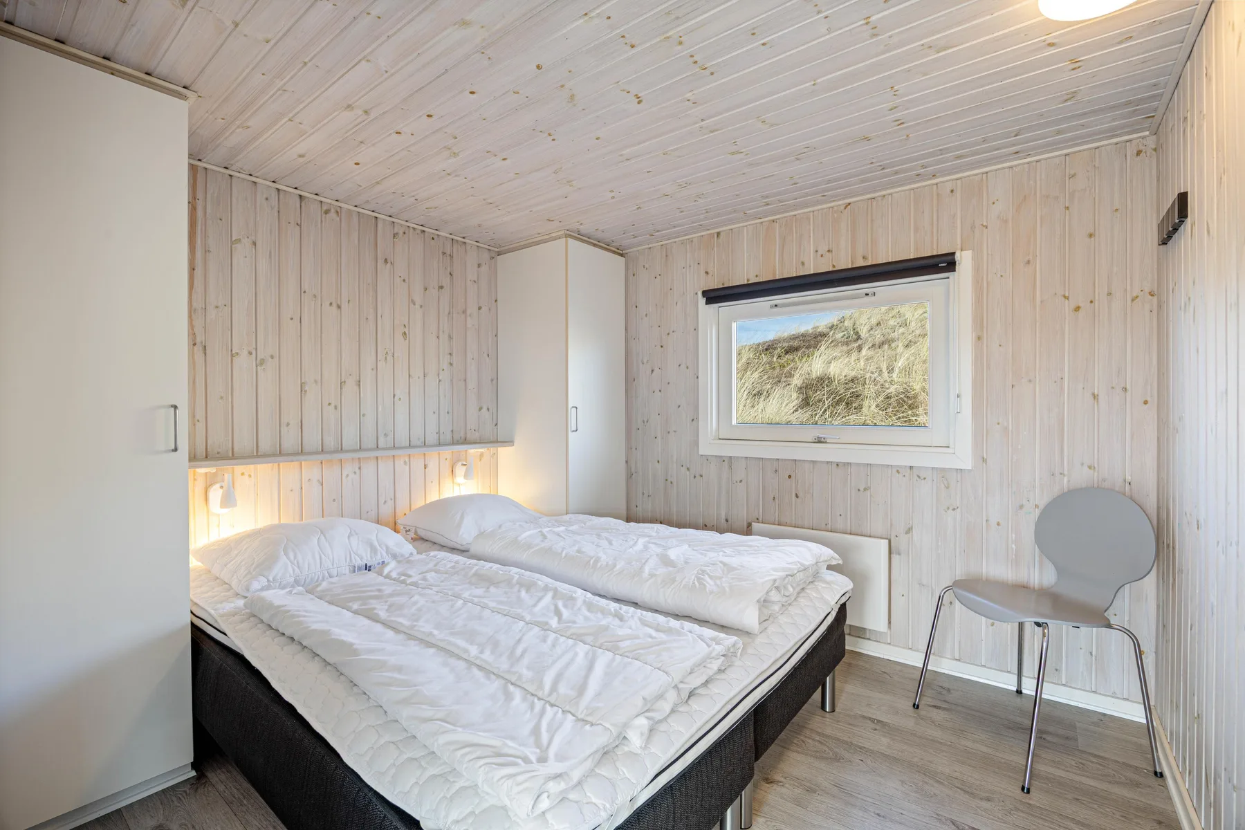 Un dormitorio con una cama doble y una ventana con vistas a dunas cubiertas de hierba.