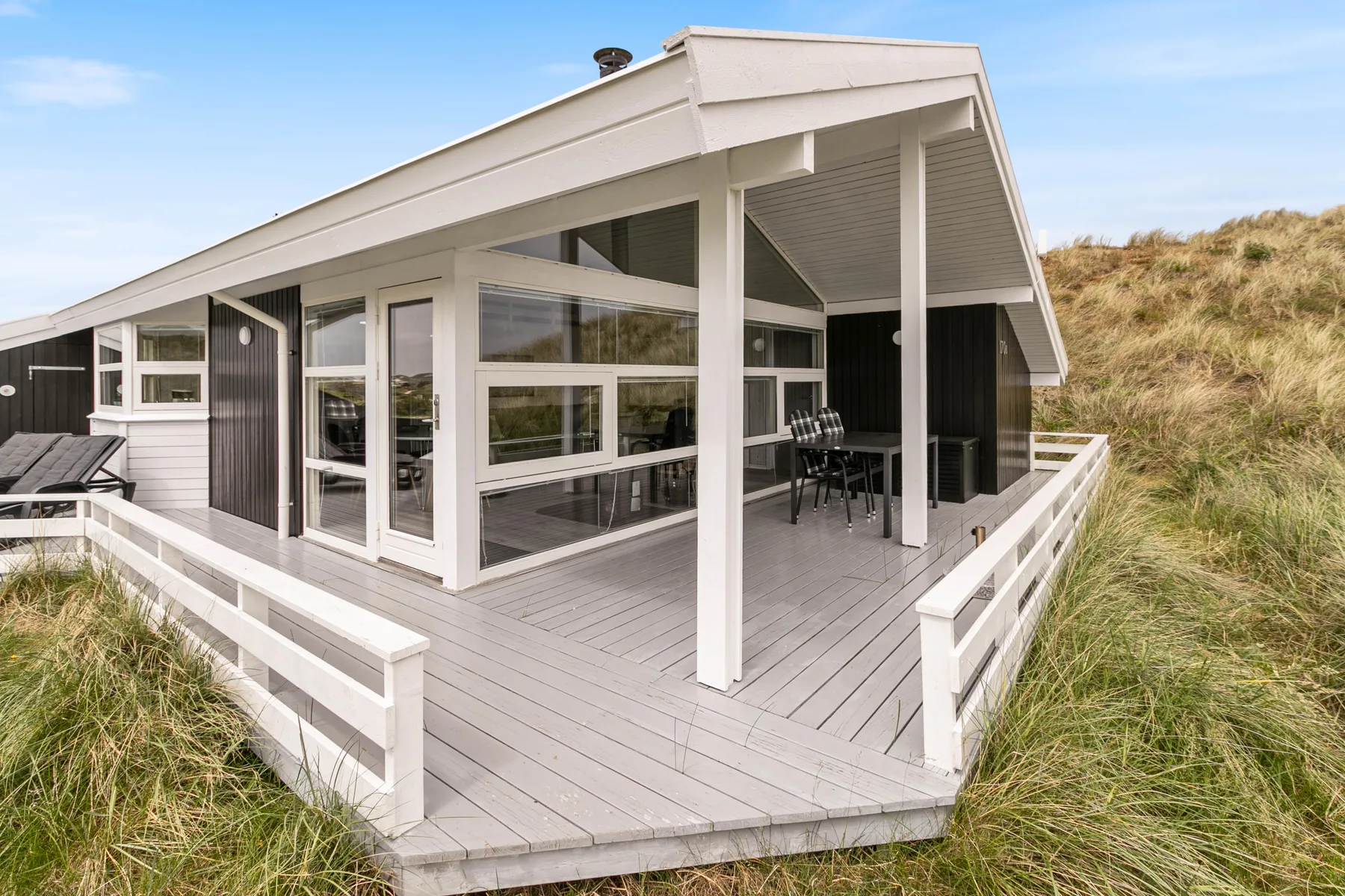 Una casa moderna con una amplia terraza rodeada de hierba de dunas.