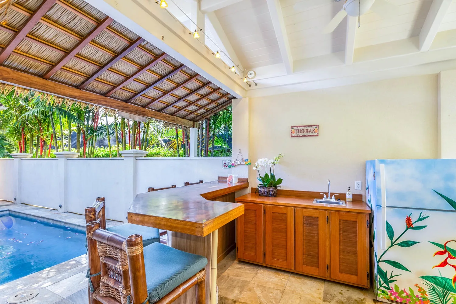 Un bar cubierto junto a la piscina, con una barra de madera y arte tropical colorido.