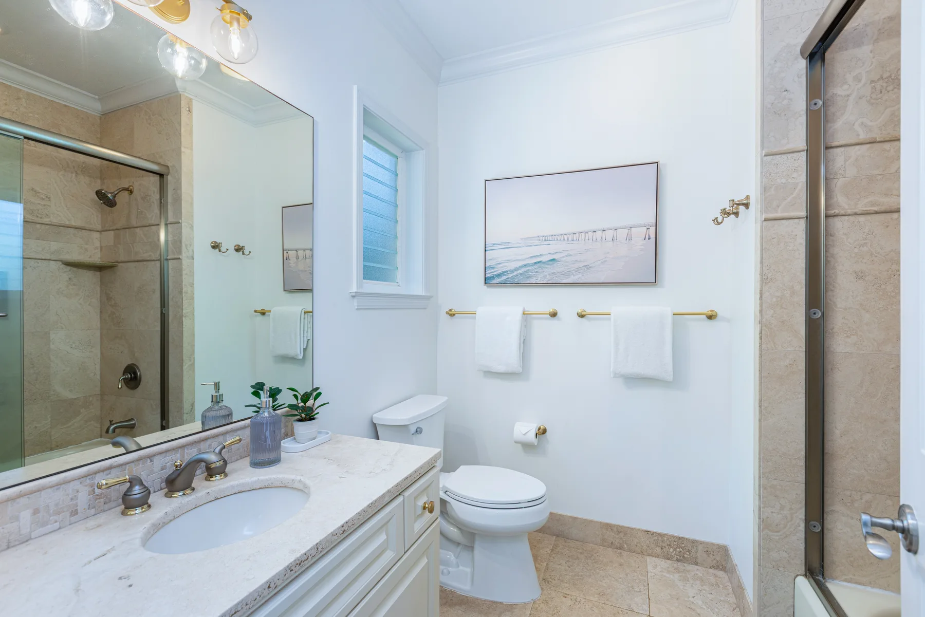 Un baño luminoso con lavabo, inodoro y una imagen enmarcada de la playa.
