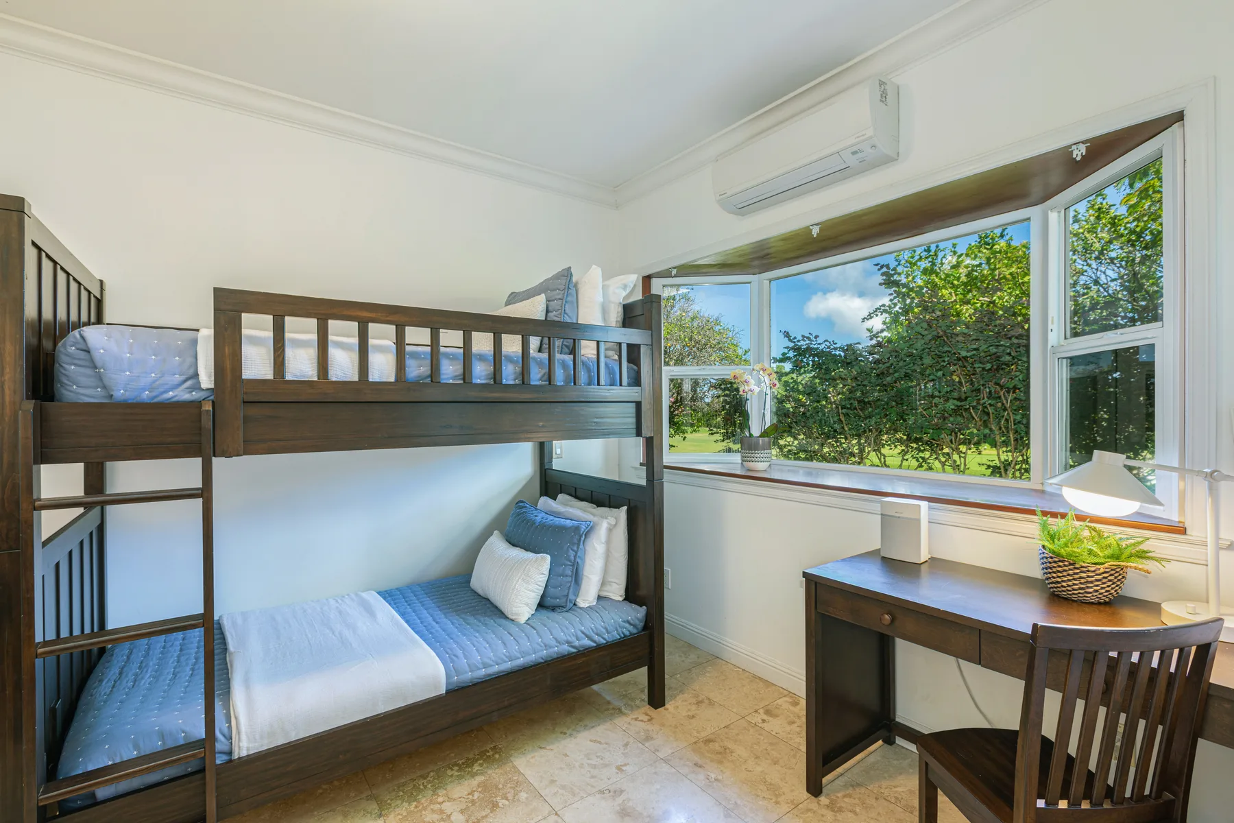 Una zona para dormir con literas junto a un escritorio y amplias ventanas con vistas a la vegetación.
