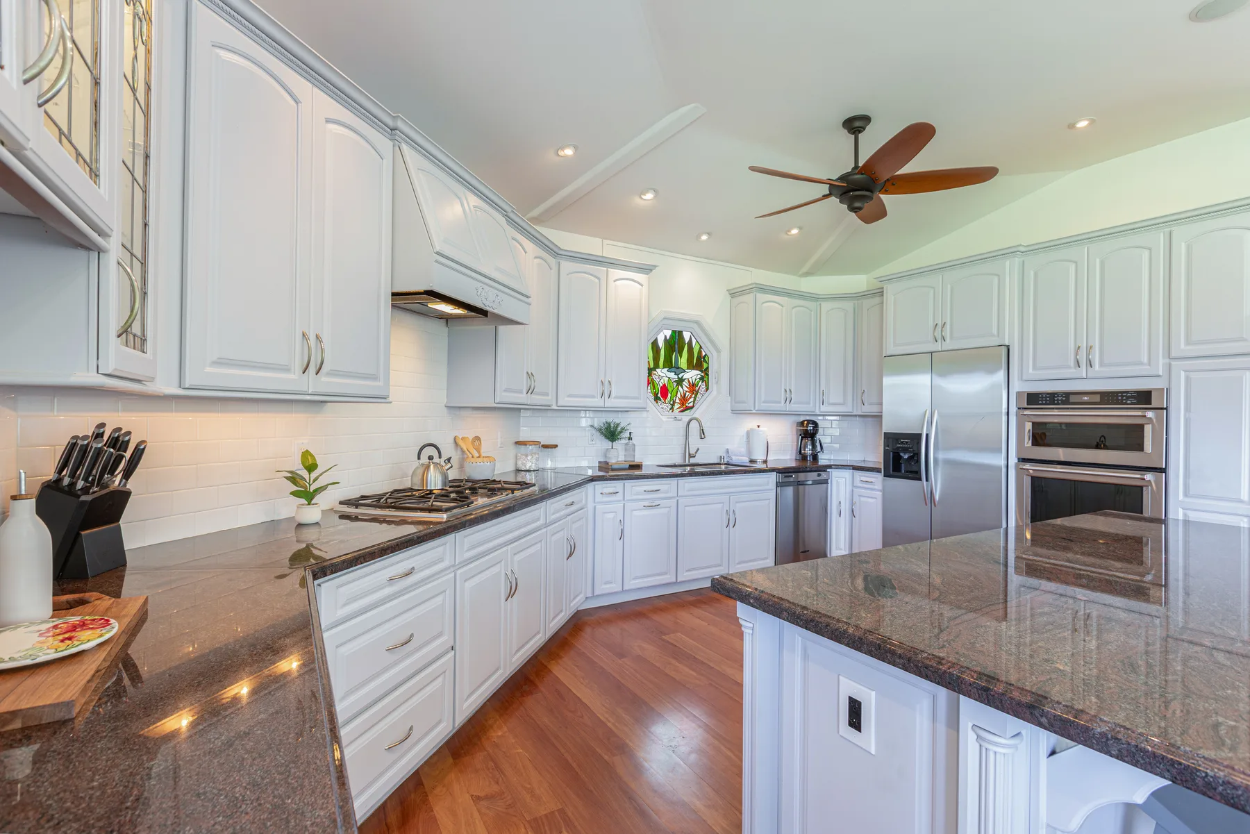 Una cocina luminosa con gabinetes blancos, una isla central y piso de madera.