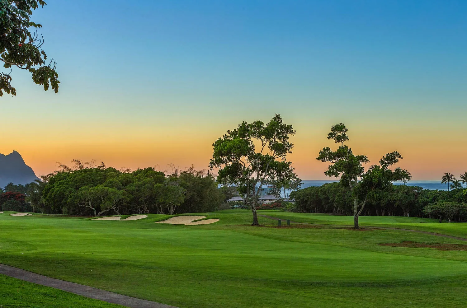 Un campo de golf se extiende por un paisaje verde bajo un cielo de atardecer colorido.