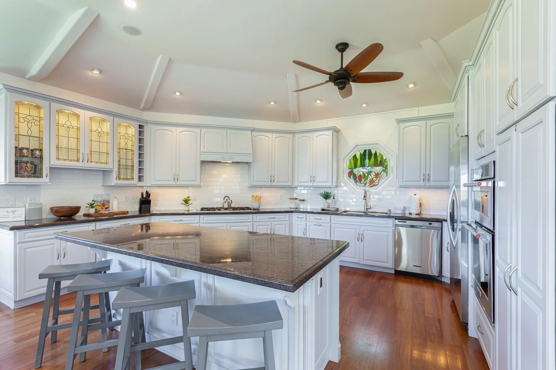 Una cocina luminosa con gabinetes blancos, una isla grande y un ventilador de techo.