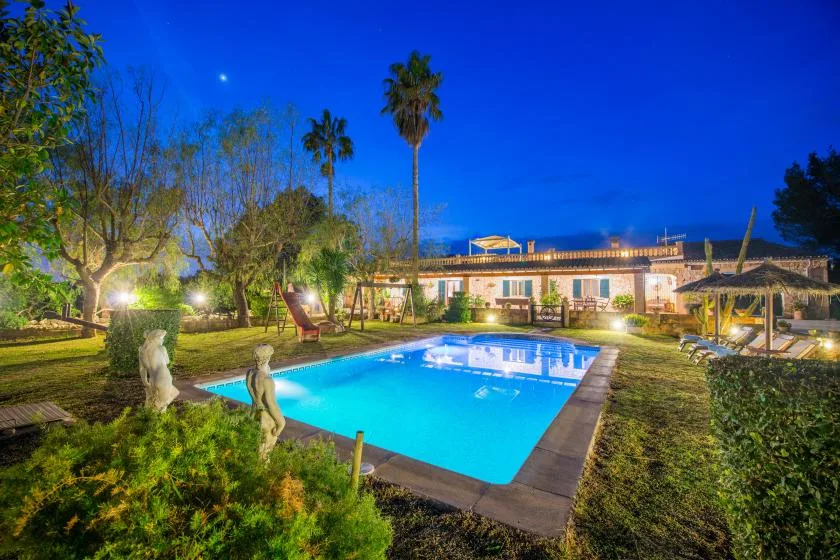 An outdoor swimming pool sits in a landscaped garden beside a low building.
