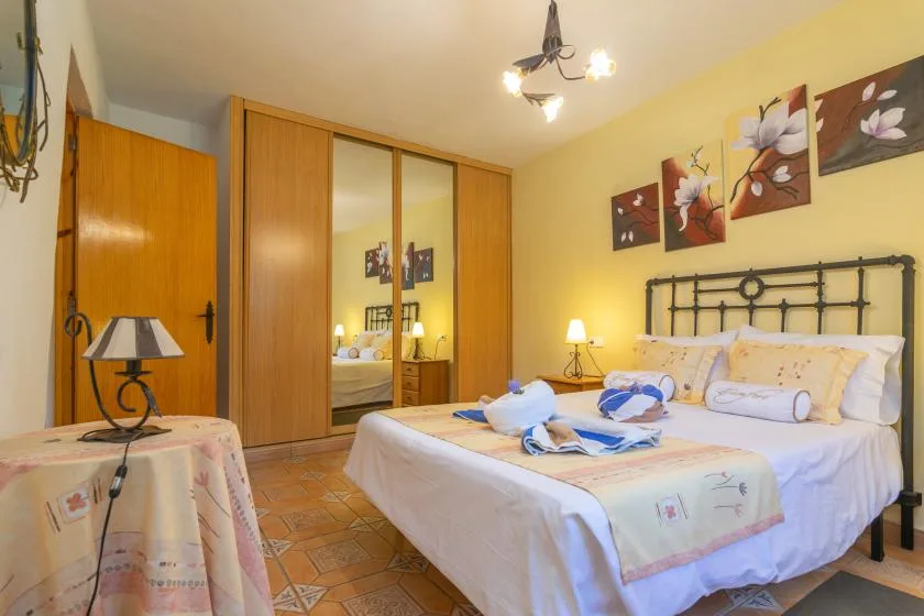 A bedroom with a double bed, mirrored wardrobe, and floral wall art.