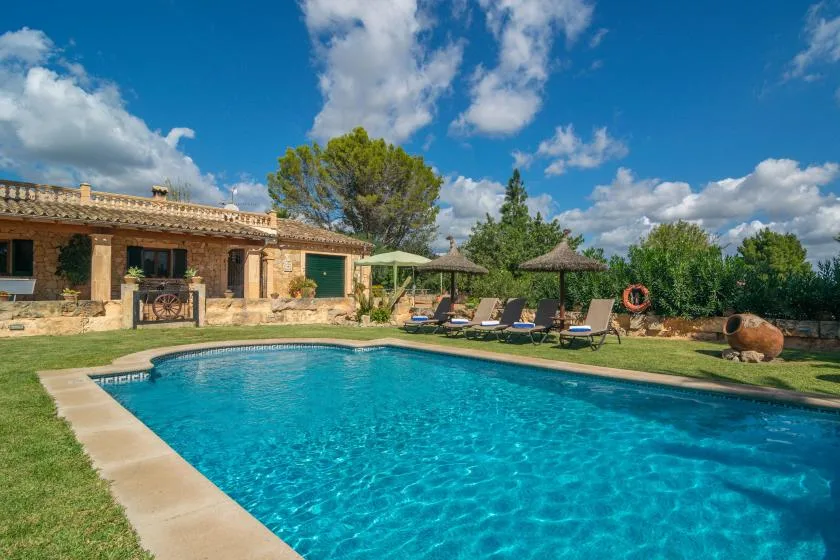 An outdoor swimming pool beside a low stone building and shaded seating.