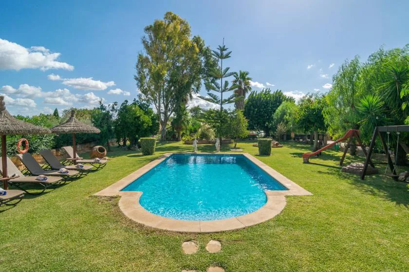 A swimming pool sits in a grassy garden with trees and outdoor seating.