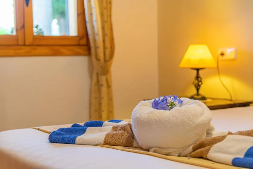 A bedroom with folded towels on the bed and a lit bedside lamp.
