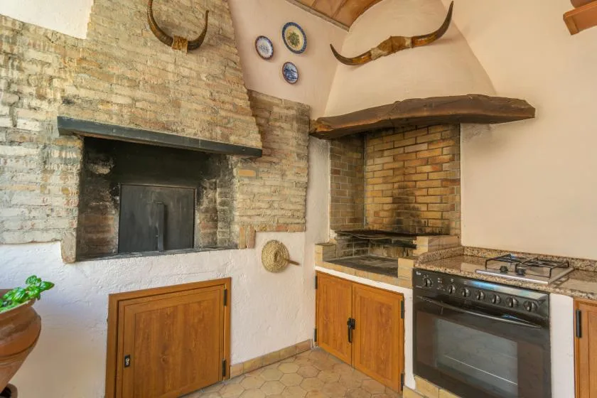 A rustic kitchen with a brick fireplace, wooden cabinets, and a stove.