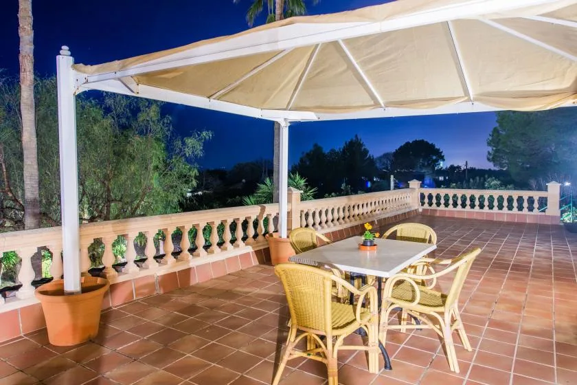 A tiled outdoor terrace has a table and seating beneath a large canopy.