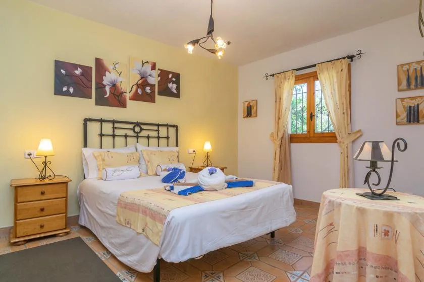 A bedroom with a neatly made bed, bedside tables, and a window with curtains.