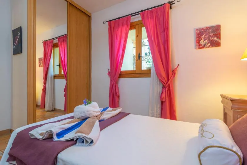 A bedroom with a bed beneath a window framed by bright pink curtains.