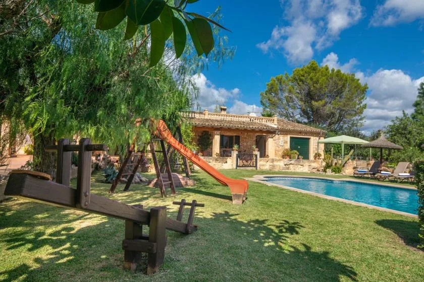 Outdoor pool and garden area with seating and a play structure beside a stone building.