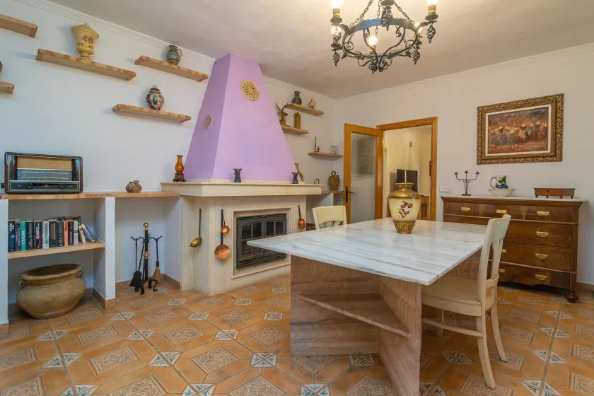 A dining room with a large table, fireplace, and wall shelves.