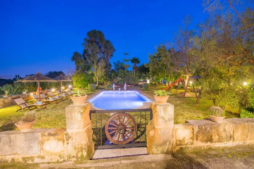 An outdoor swimming pool is surrounded by garden seating and trees.