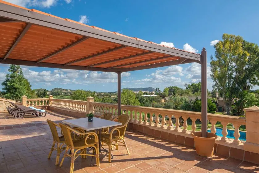 A covered terrace overlooks a pool and green hills.