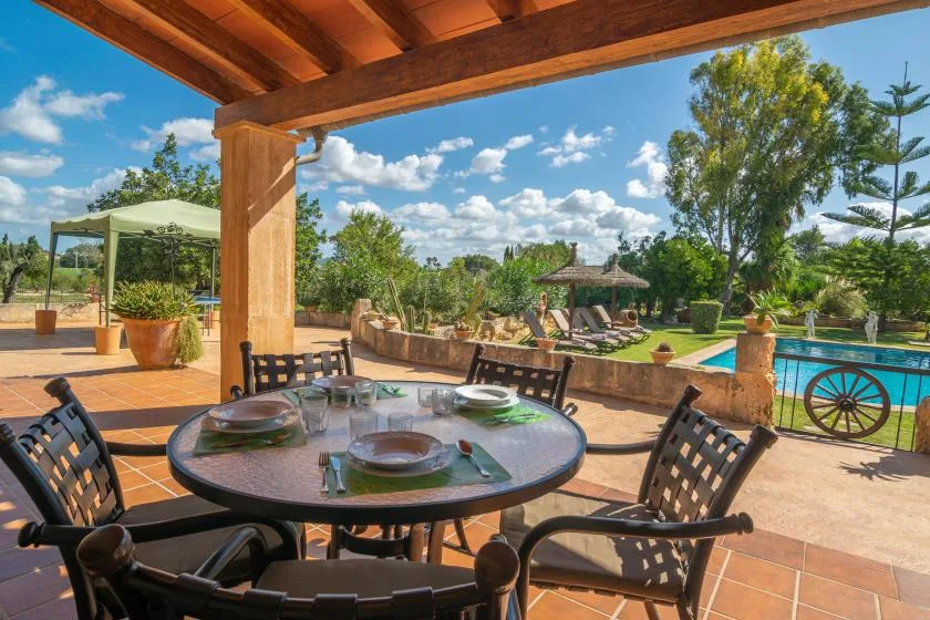 A covered outdoor dining area overlooks a swimming pool and landscaped garden.
