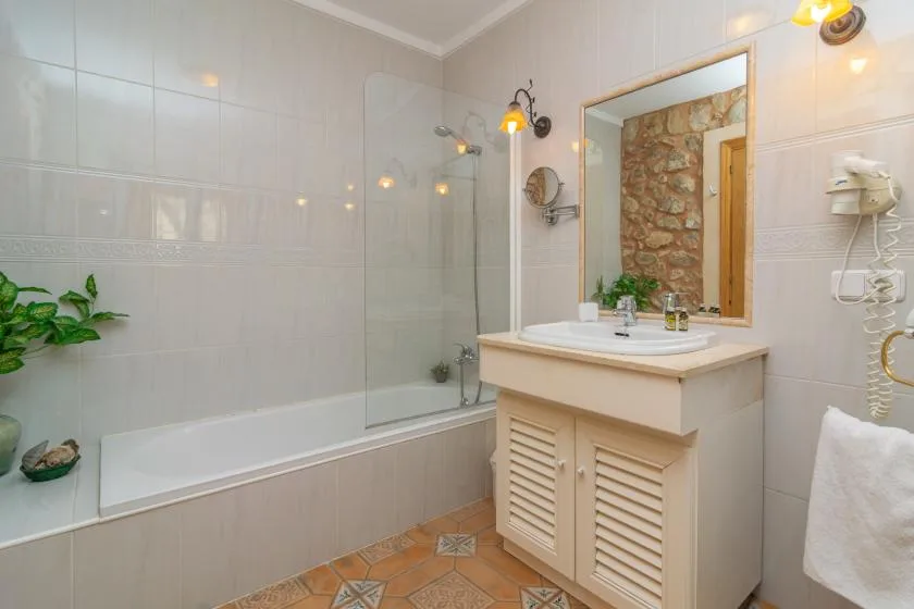 A tiled bathroom with a bathtub, glass shower screen, and sink vanity.