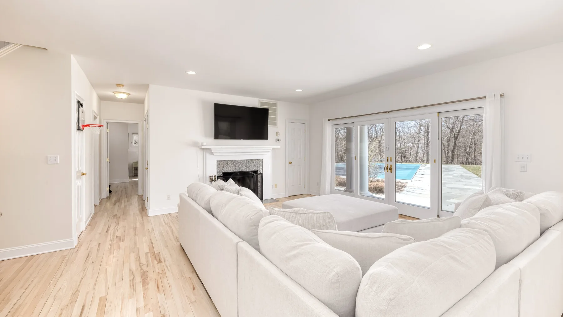 Una sala luminosa con asientos blancos, una chimenea y grandes ventanales con vista a una piscina.