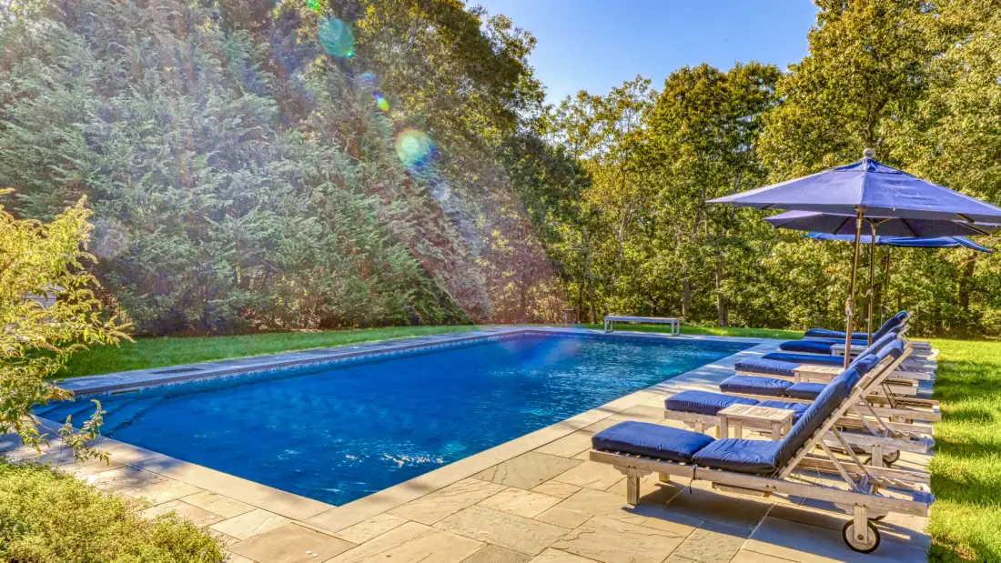 Una piscina al aire libre está rodeada de tumbonas y árboles frondosos.