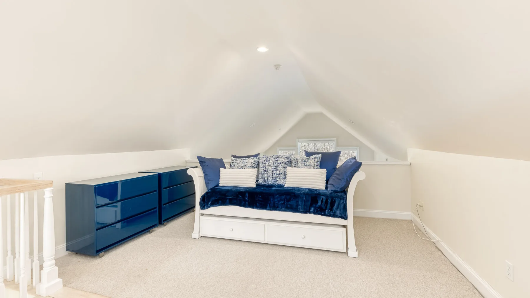 Un dormitorio abuhardillado luminoso con un diván azul y un mueble bajo.