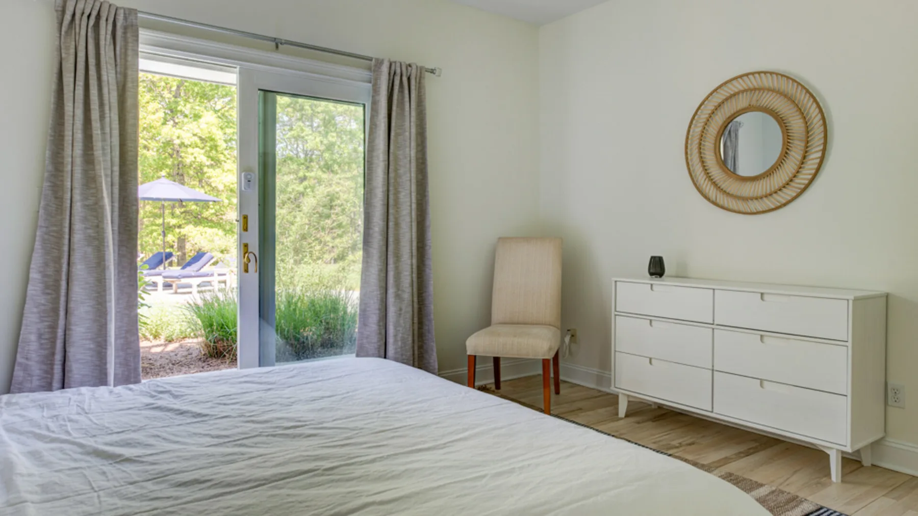 Un dormitorio luminoso con una cama, una cómoda y puertas de vidrio hacia la vegetación.