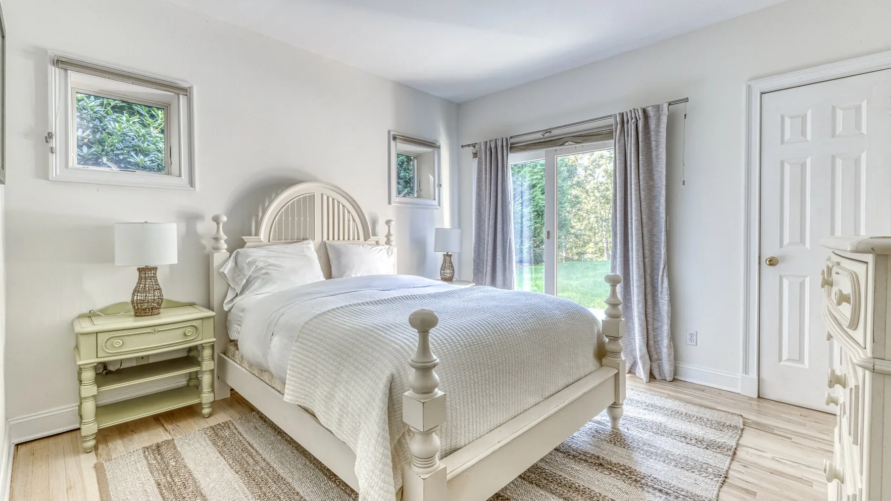 Un dormitorio luminoso con una cama blanca junto a puertas de vidrio con cortinas.