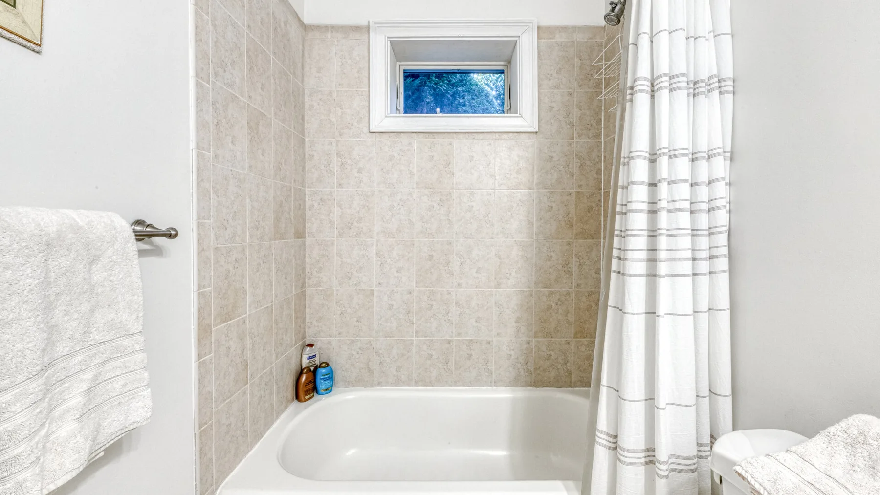 Un baño con azulejos tiene una bañera y una cortina de ducha a rayas.