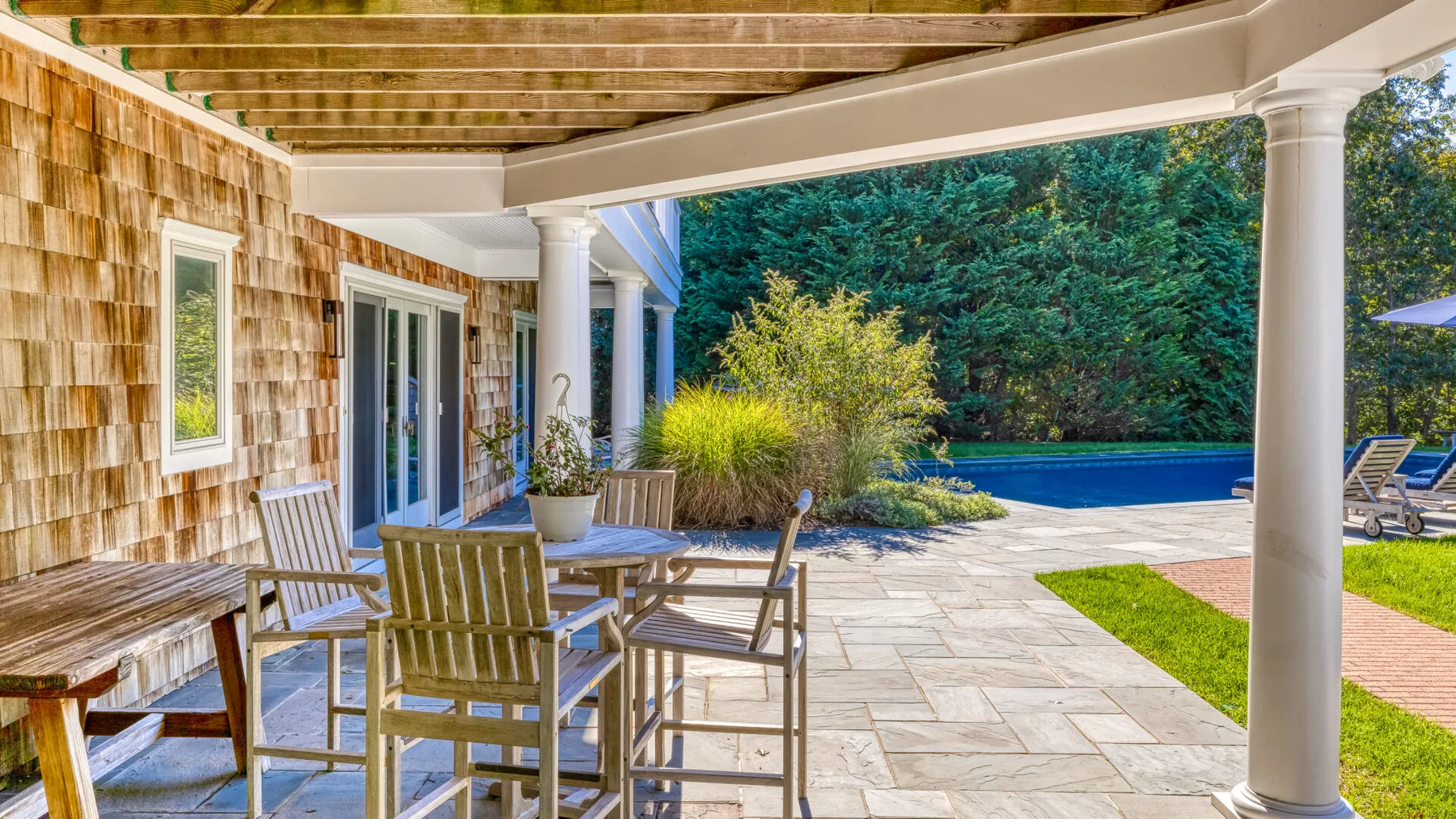 Un patio cubierto con asientos al aire libre da a una piscina y un jardín.