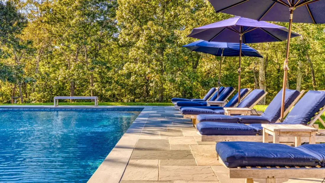 Una piscina al aire libre con tumbonas acolchadas y sombrillas junto a la terraza.