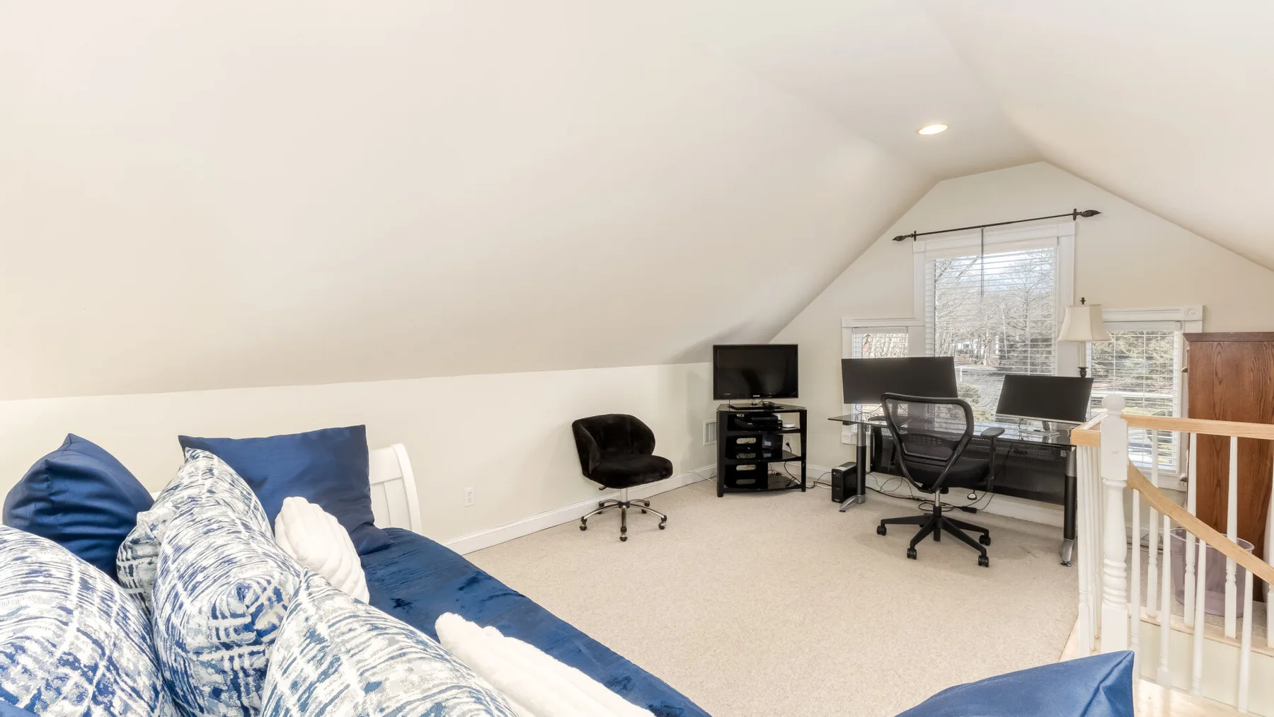 Dormitorio abuhardillado con una cama junto a un escritorio y una computadora.