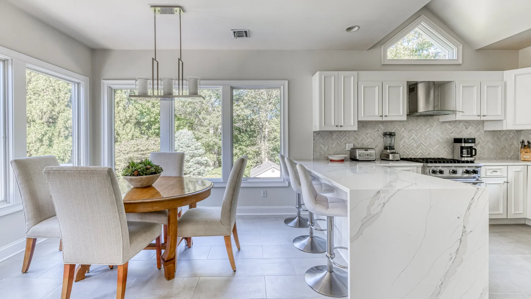 Una cocina y comedor luminosos con una isla de mármol y una mesa de comedor de madera.