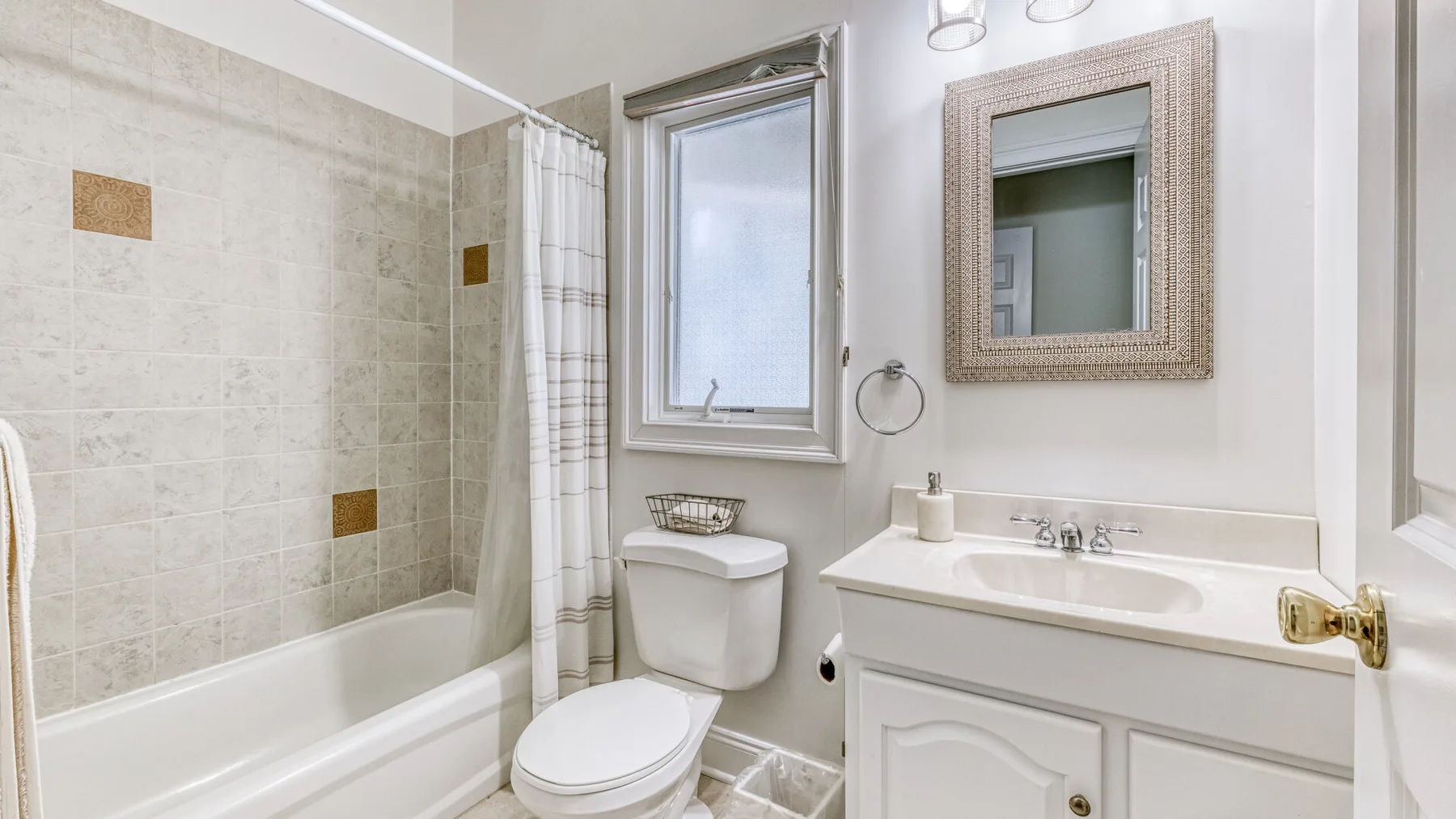 Un baño luminoso con bañera, inodoro y lavabo bajo una ventana.