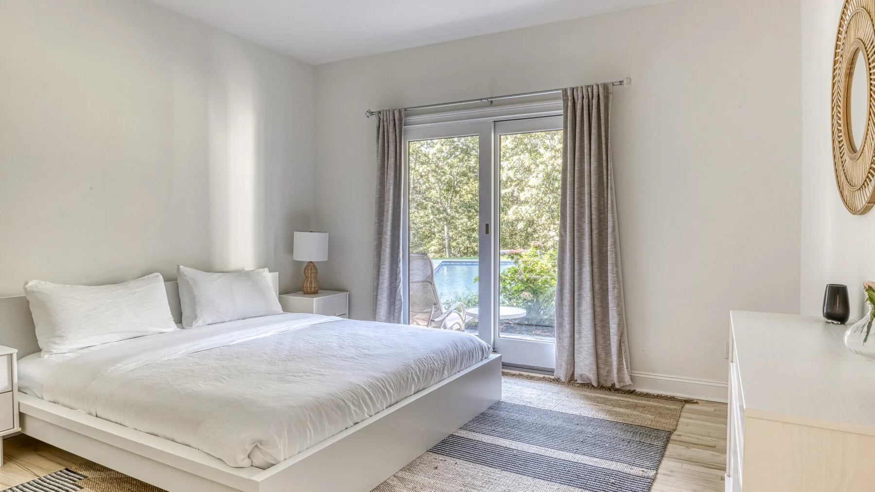Un dormitorio luminoso con una cama tendida junto a puertas de cristal y cortinas.